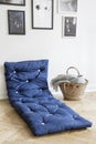 Navy blue mattress next to basket in white interior with gallery of posters on the wall. Real photo