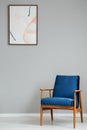 Navy blue wooden armchair in simple grey living room interior with poster on the wall