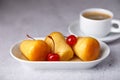 Neapolitan Rum baba or baba au rum on a white plate with a cocktail cherry and a cup of coffee. Small yeast cakes soaked in rum