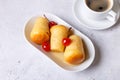 Neapolitan Rum baba or baba au rum on a white plate with a cocktail cherry and a cup of coffee. Small yeast cakes soaked in rum