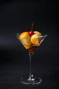 Neapolitan Rum baba or baba au rum in a martini glass with a cocktail cherry on a black background. Small yeast cakes.