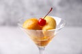 Neapolitan Rum baba or baba au rum in a martini glass with a cocktail cherry on a gray background. Small yeast cakes.