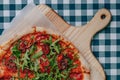 Neapolitan spicy pizza with ham, cheese, arugula, basil, tomatoes, pepperoni pepper sprayed with cheese on a wooden board on a Royalty Free Stock Photo