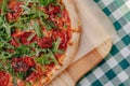 Neapolitan spicy pizza with ham, cheese, arugula, basil, tomatoes, pepperoni pepper sprayed with cheese on a wooden board on a Royalty Free Stock Photo