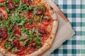 Neapolitan spicy pizza with ham, cheese, arugula, basil, tomatoes, pepperoni pepper sprayed with cheese on a wooden board on a Royalty Free Stock Photo