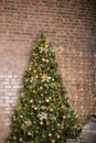 Near the brick wall is a beautiful new year`s green pine tree, decorated with different balls, flowers and a garland on the wall Royalty Free Stock Photo