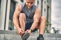 A man with wired headphones in a light athletic uniform ties a lace on a shoe for running. Sport concept