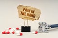 Near the stethoscope are pills and a clip with a cardboard sign - pain in the hand Royalty Free Stock Photo