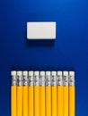 A neat row of yellow pencil rubber erasers, pointing to a white rectangular rubber eraser on a blue background