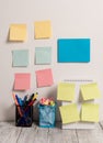 Neat Workplace with Blue Card and 10 Empty Colored Stick Pad Notes Put on Both White Wall and Open Spiral Notebook with