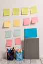 Neat Workplace with 12 Empty Colored Stick Pad Notes and Blue Card Put on White Wall and 2 Full Pencil Pots next to Grey