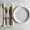 A neatly arranged table setting on a white marble surface. A beige cloth napkin is folded Royalty Free Stock Photo