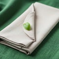 A neatly folded beige napkin with soft, textured fabric is placed on a green surface. A Royalty Free Stock Photo