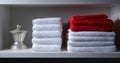 Neatly folded white and red towels stacked on a white shelf with a decorative silver container beside them in a minimalist setting Royalty Free Stock Photo