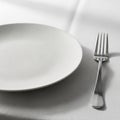 A neatly set table features a white round ceramic plate with a textured surface on a white tableclot Royalty Free Stock Photo