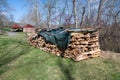 Neatly stacked cordwood with tarp and colonial barn background