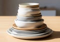 A neatly stacked set of ceramic dishes and bowls on a wooden table. The stack includes white, gray, Royalty Free Stock Photo
