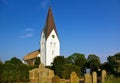 Nebel, Amrum, Germany - June 1st, 2016 - Historic whitewashed church in front of a blue sky with graveyard and ancient headstones