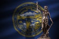 Nebraska US state flag with statue of lady justice and judicial scales in dark room. Concept of judgement and punishment