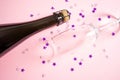 Neck of a bottle of champagne and a glass on a pastel pink background. Royalty Free Stock Photo