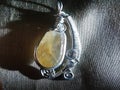 Necklace jewelry. Silver wire with a flat yellow calcite crystal on a shiny fabric.