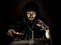 Necromancer casts spells from thick ancient book by candlelight on a dark background Royalty Free Stock Photo