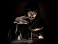 Necromancer casts spells from thick ancient book by candlelight on a dark background Royalty Free Stock Photo