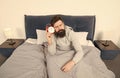 Need more sleep. Get up with alarm clock. Tips for waking up early. Man bearded sleepy face bed with alarm clock in bed