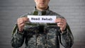 Need rehab words written on sign in hands of male soldier, social support