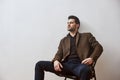 Need a rest. Pensive brunette man in brown jacket and blue trousers sitting on the chair and looking away over white Royalty Free Stock Photo