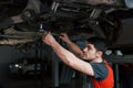 Need a solid hand. Man at the workshop in uniform fixes broken parts of the modern car