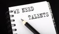 WE NEED TALENTS written text in small notebook on a black background