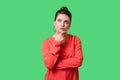 Need to think! Portrait of pensive elegant young woman with bun hairstyle, big earrings and in red blouse. indoor studio shot Royalty Free Stock Photo