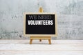 We need Volunteers text on the blackboard set on wooden floor and brick background Royalty Free Stock Photo