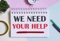 WE NEED YOUR HELP text written on a notebook with pencils, magnifier Royalty Free Stock Photo