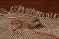 Needle with brown thread and steel thimble on natural linen texture for background. Close. Royalty Free Stock Photo
