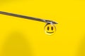 Needle with a drop and a smile on yellow background. Drugs from syringe Royalty Free Stock Photo