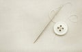 The needle and thread lie on a white cloth. Button on clothes. Seamstress and tailor tools