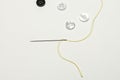 Needle with yellow thread threaded together with some white buttons and one black on a smooth surface Royalty Free Stock Photo