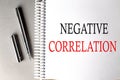 NEGATIVE CORRELATION text on a notebook with pen on grey background