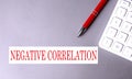 NEGATIVE CORRELATION text written on a gray background with pen and calculator