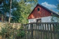 Neglected abandoned house with an old fence among grass and trees. Rural landscape