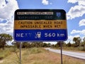 A neglected sign indicating an unsealed road with next fuel station 560 kilometers away