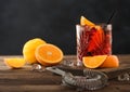 Negroni cocktail in crystal glass with orange slice and fresh raw oranges on chopping board with strainer on wooden background