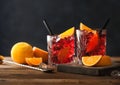 Negroni cocktail in crystal glasses with orange slice and fresh raw oranges on chopping board with strainer on wooden background