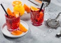 Negroni cocktail in crystal glasses with orange slice and fresh raw oranges with strainer on light background