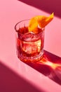 Negroni cocktail stands on a pink background with bold shadows, illuminated by the warm glow of the setting sun Royalty Free Stock Photo