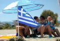 Little Greek flag in sand isolated with blurred people