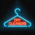 Neon dry cleaners glowing sign with hanger on a dark brick wall background.