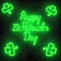 Neon glowing happy saint patricks day with clover leaves on a dark brick wall background.